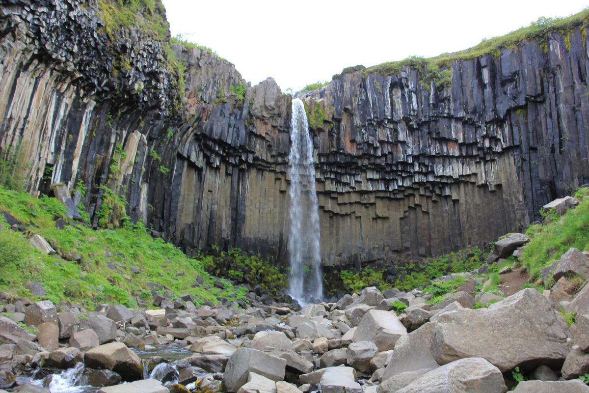 Waterval komt van hoog tussen de zwarte basaltrotsen naar beneden.