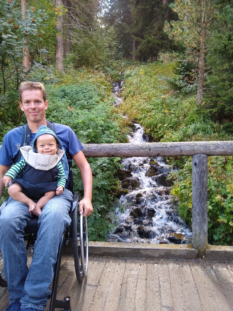 Thomas met zijn zoontje op schoot, op een brug boven een bergrivier