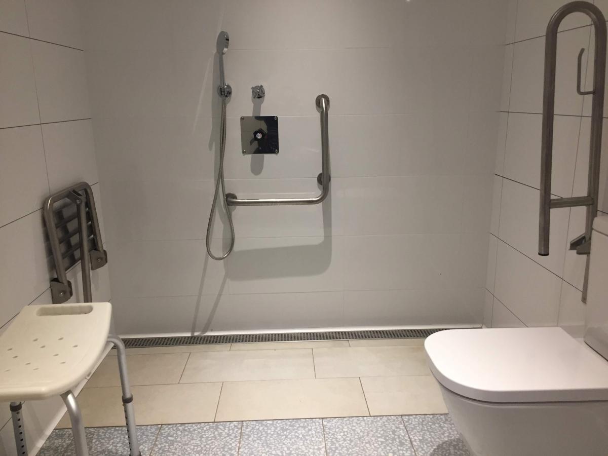  het toilet heeft een steunbeugel. In de douche zien we een vast douchezitje met handgrepen én een tabouret zonder leuning. De douchekop is afneembaar.