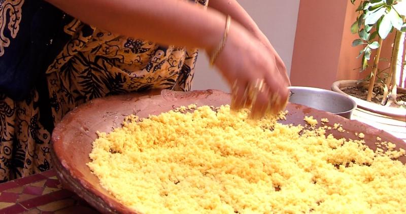 De kokkin roert met de hand in een grote pan met goudgele couscous.