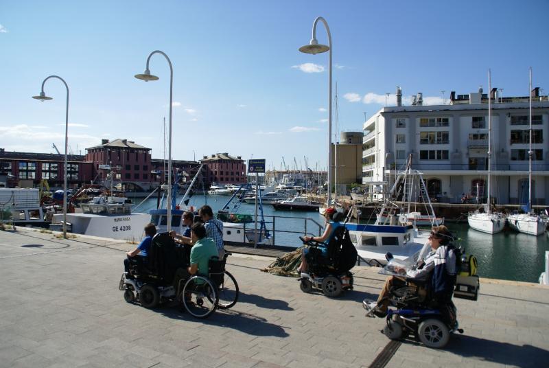 Zes vrienden, allen rolstoelgebruikers, op wandel langs de jachthaven van Genua.