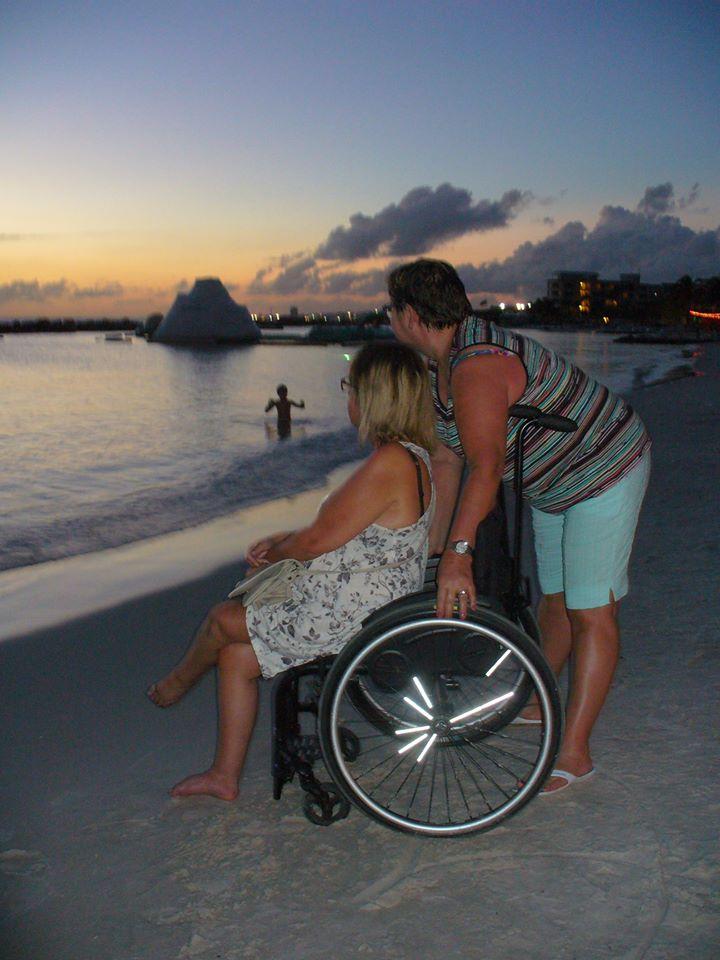 Nadine (met rolstoel) en Lia bij zonsondergang op het strand.