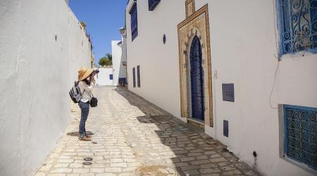 Een toerist fotografeert de helblauwe deur van een wit huis in een zonovergoten straatje in Tunis.