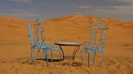 Twee sierlijke azuurblauwe stoelen en een rond tafeltje staan klaar voor de thee in een woestijnlandschap.