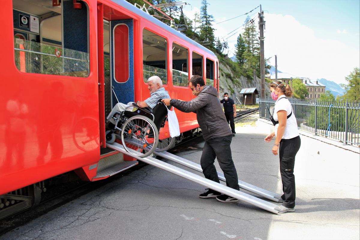 Jozef wordt met de rolstoel op de rode trein geholpen.