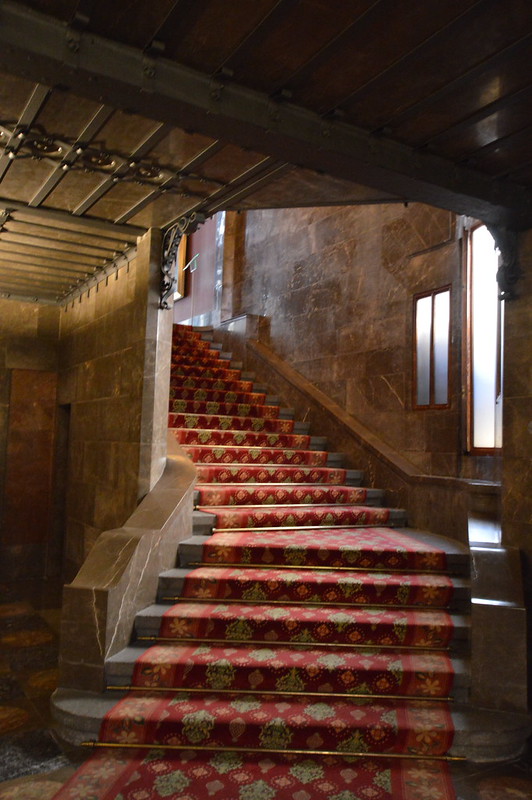 Traphal in Palau Güell. De trap is bekleed met een rood tapijt met gouden motieven.
