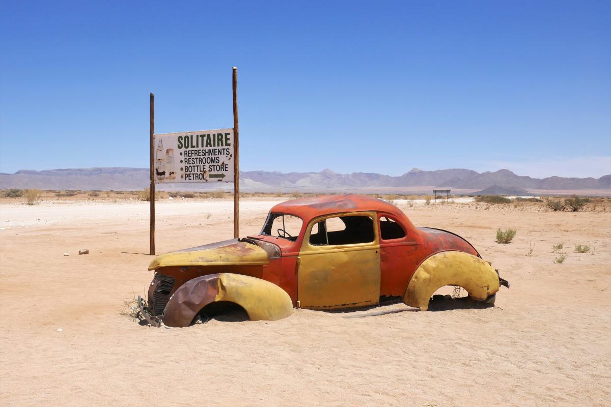 Een autowrak in het zand, met een wegwijzer naar Solitaire. Desolater wordt het niet.