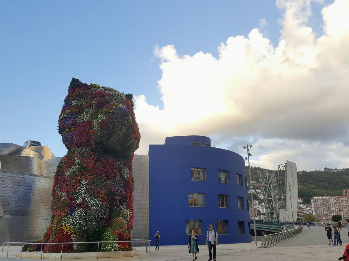 Ingang van het Guggenheim-museum met reuzengroot Puppy-sculptuur van rode, witte, paarse, oranje, roze en gele bloemen.