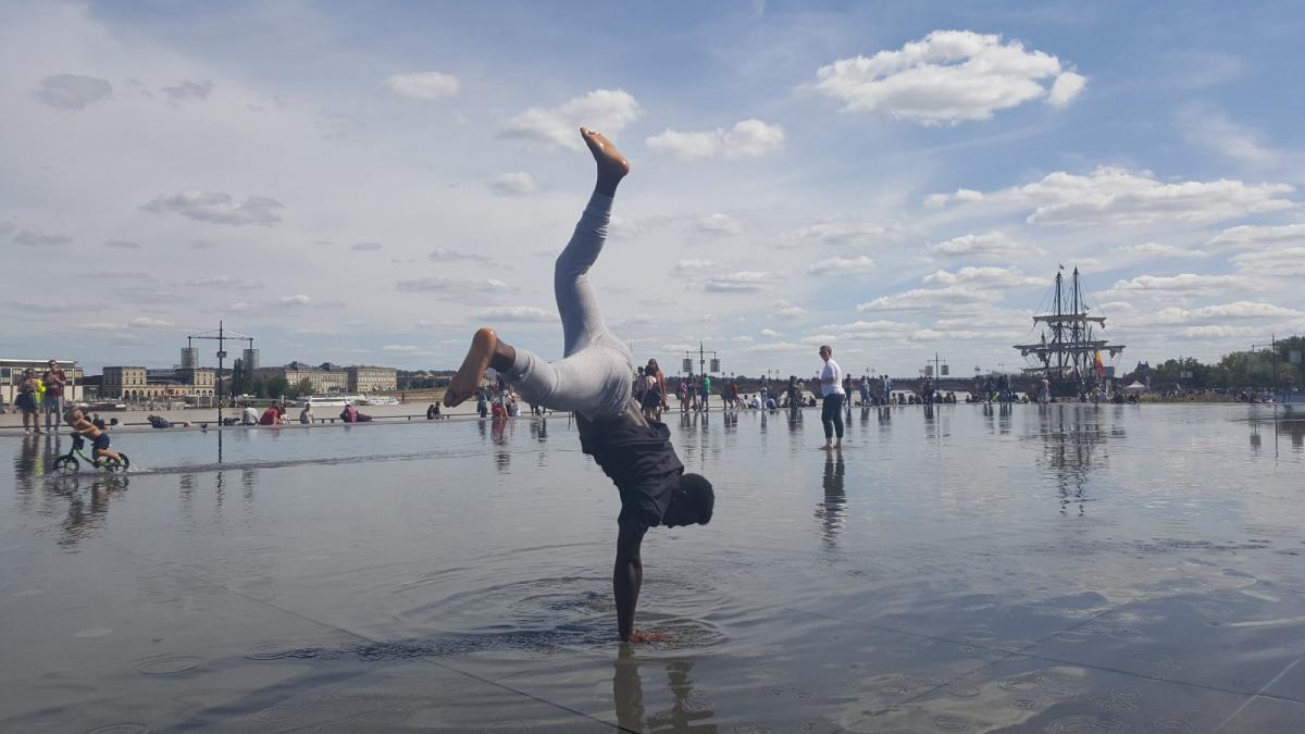 Breakdancer op de waterspiegel, met driemaster op de achtergrond