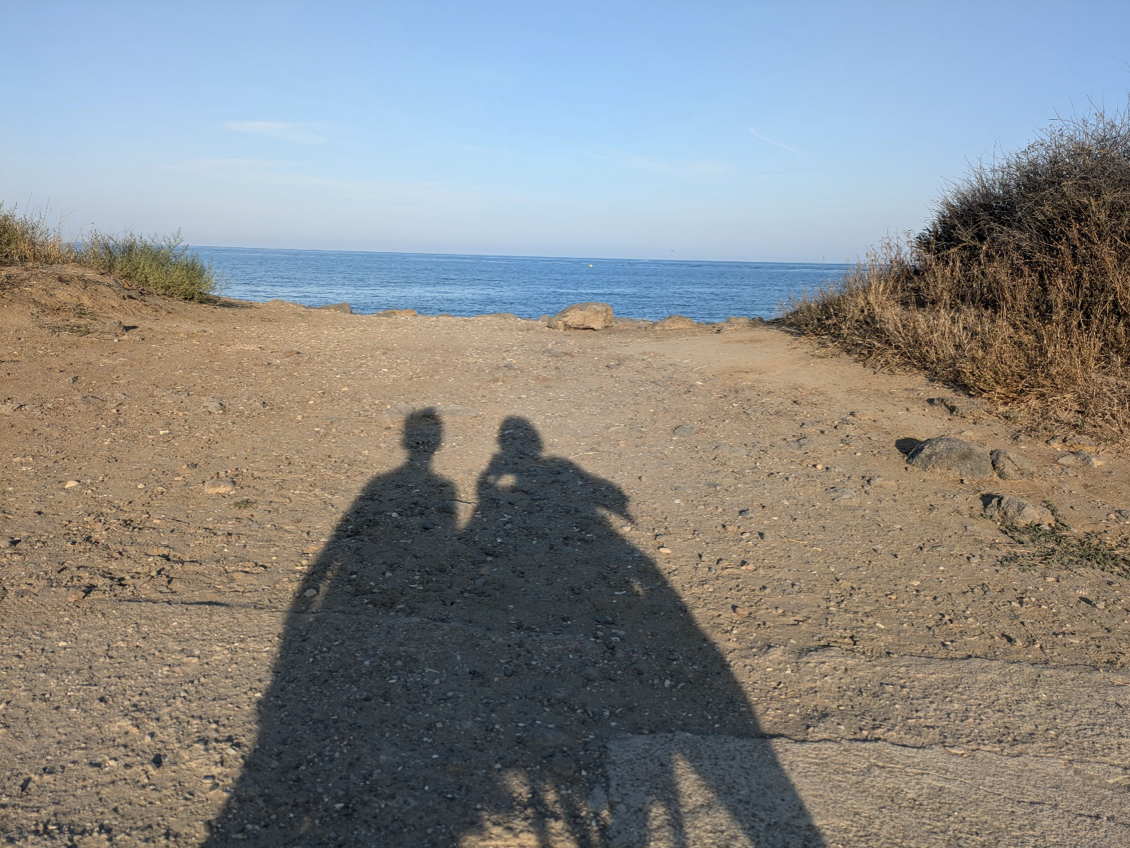 Schaduw van twee rolstoelers op het strand.
