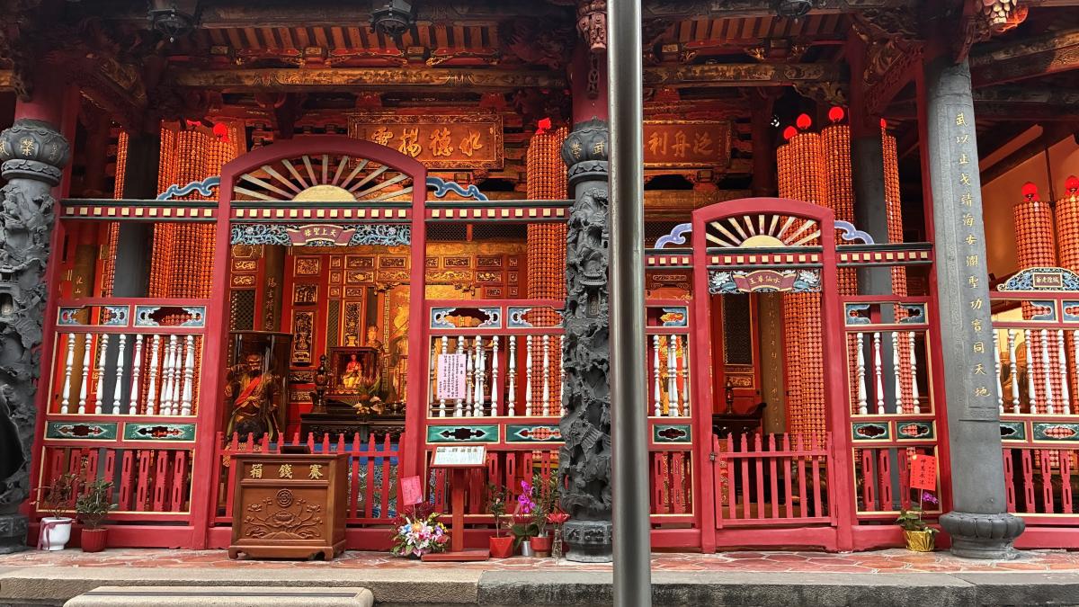 Roodgelakt hout en zuilen van offerkaarsjes omlijsten de beelden in de tempel.