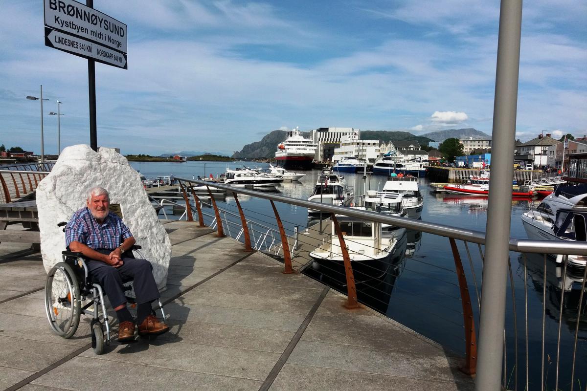 Jozef poseert op de kade van Brønnøysund. Op de achtrgrond ligt een cruiseschip te wachten om verder te varen.