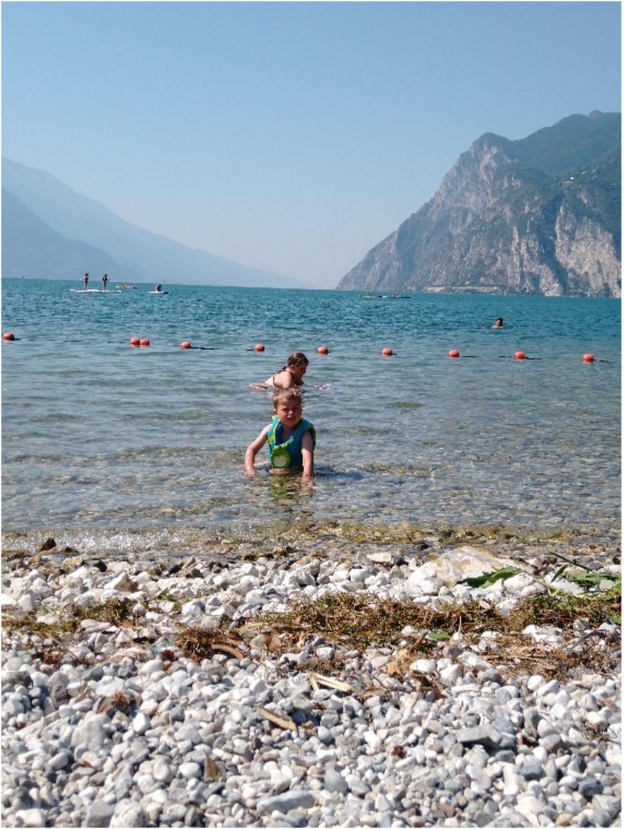 Kinderen spelen in een afgebakende zone van het Gardameer. Op de voorgrond zien we het keienstrand.