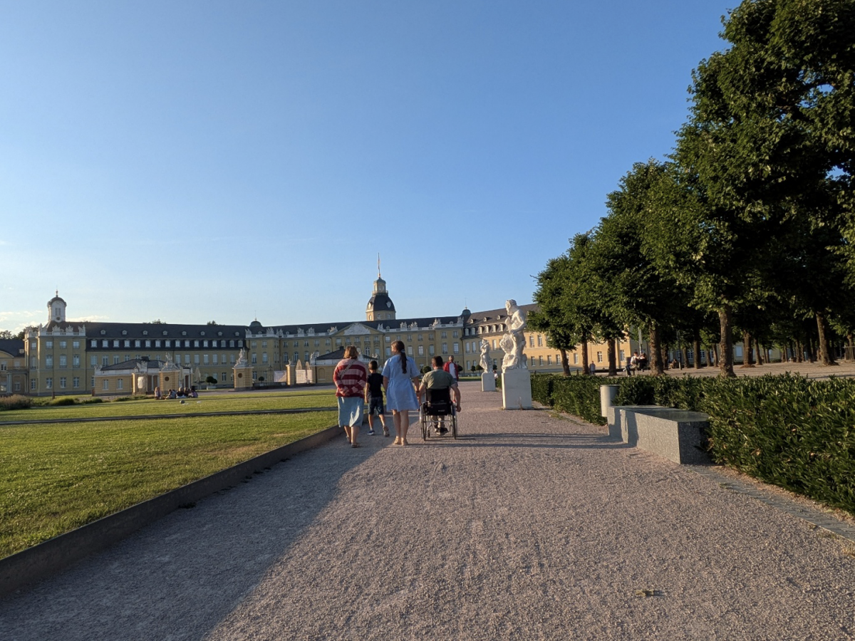 Eva, Thomas en de kinderen van de rug gezien op de lange oprit naar een kasteel in classissistische stijl. Langs het pad staan witmarmeren standbeelden.