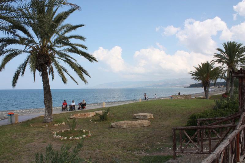 Foto uit Cyprus: drie rolstoelers wandelen onder de blauwe lucht langs de Middellandse Zee.