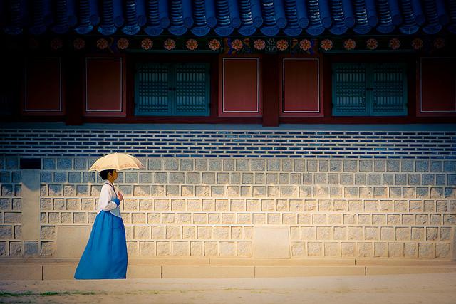 Een poëtische foto uit Seoul, Korea: een vrouw met blauwe jurk en witte parasol wandelt voorbij.