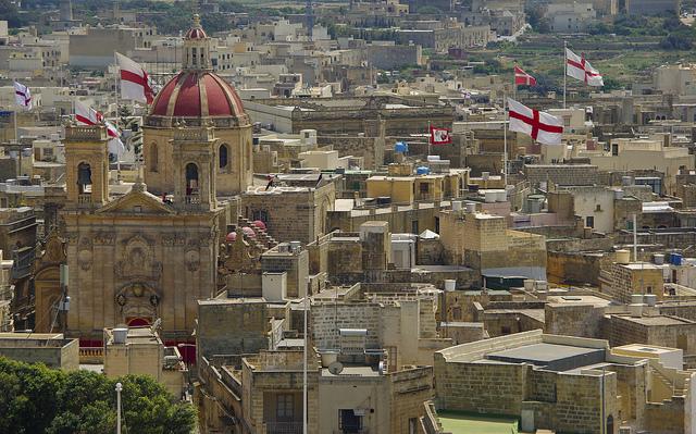 Zicht op de stad, met veel Maltese vlaggen en de rode dakkoepel van de kathedraal van Gozo.