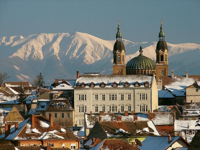 Twee torens en het koepeldak van de orthodoxe kathedraal, tegen een achtergrond van besneeuwde bergtoppen.