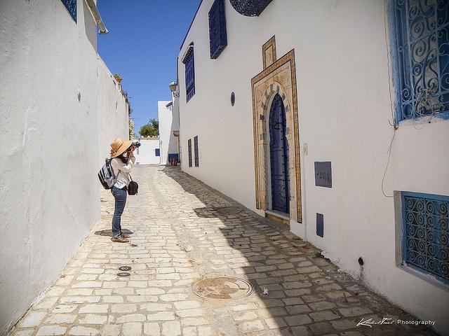 Een toerist fotografeert de helblauwe deur van een wit huis in een zonovergoten straatje in Tunis.