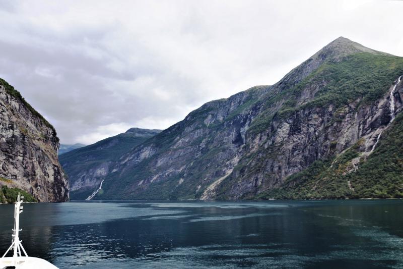 Een wit schuimende waterval bereikt via ruwe donkere rotsen het vredige staalblauwe water van Geirangerfjord.