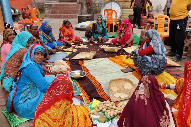 Vrouwen in kleurige kleren in een kring op een vloerkleed maken naan (platbrood). Kleine bolletjes deeg worden platgerold.