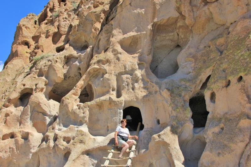 Marie-Claire zit tussen de huizenhoge kalkrotsen van Bandelier National Monument.