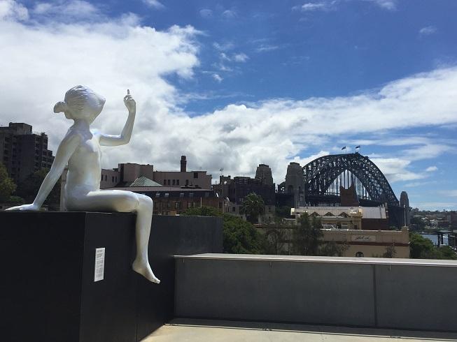 Op de achtergrond Harbour Bridge, op de voorgrond een sculptuur van een meisje dat naar de wolken wijst.