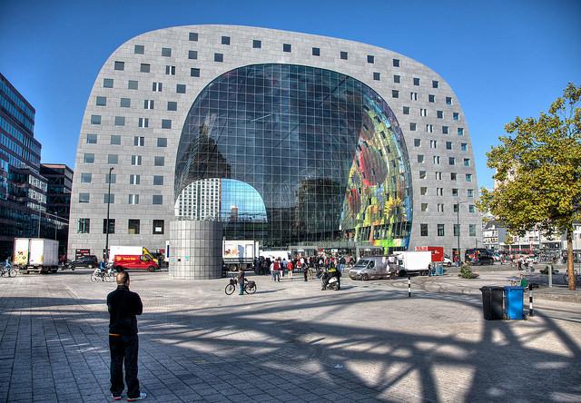 De markthal, een gebouw uit 2014, heeft een hoefijzer-vorm. Binnen zien we een glimp van een kleurig kunstwerk.