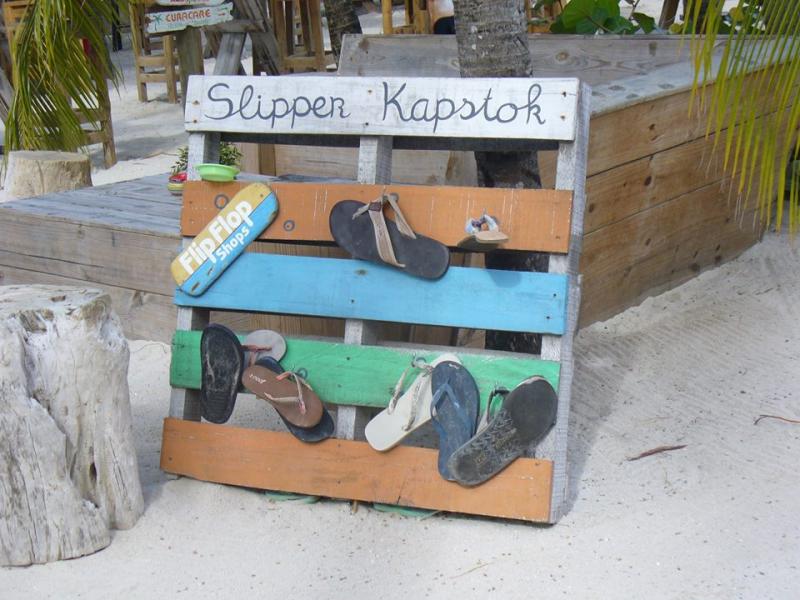 Een houten palet is omgetoverd tot een kleurige "slipperkapstok", voor wie blootvoets het strand op wil.