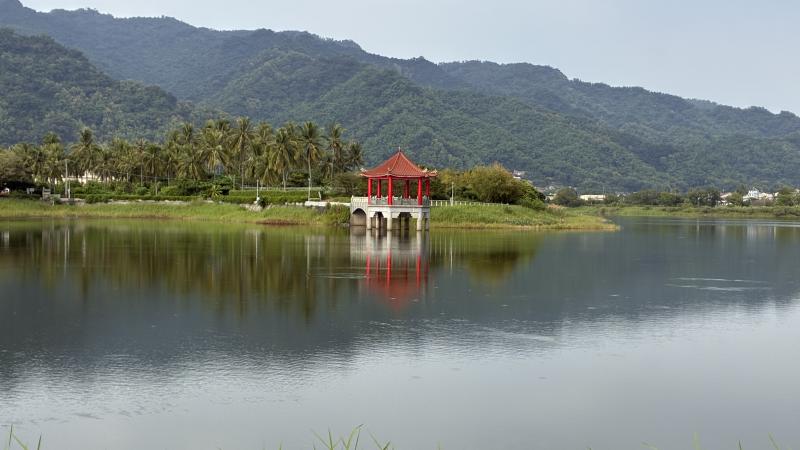 Zicht over Meinong Lake, met de bergen op de achtergrond en een rood prieel op de voorgrond.