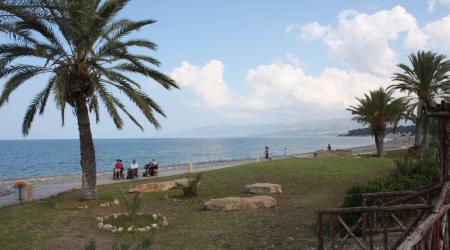 Foto uit Cyprus: drie rolstoelers wandelen onder de blauwe lucht langs de Middellandse Zee.