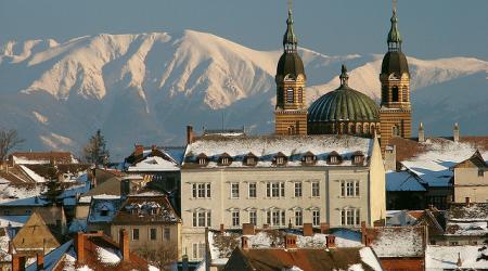 Twee torens en het koepeldak van de orthodoxe kathedraal, tegen een achtergrond van besneeuwde bergtoppen.